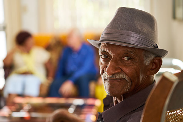 Portrait of elderly black man looking at camera in retirement home, with group of friends in background.