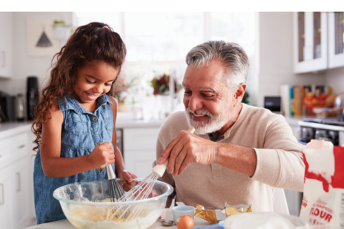grandfather mixing cake batter with granddaughter in kitchen.