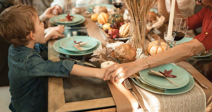 family holding hands, gathered at the table for Thanksgiving dinner.